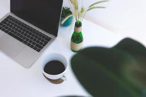 lugar de trabajo independiente, computadora portátil, taza de café y planta en maceta en la mesa blanca foto