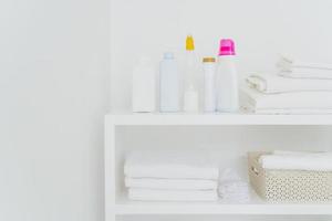 Stack of clean white towels with detergents on console isolated over white background. Fresh laundry and liquid washing in bathroom photo