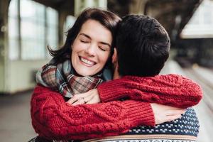 Beautiful female with happy expression, embraces her boyfriend, being glad to meet him after long seperation, closes eyes, has real feelings. Unforgettable meeting of two lovers. Happiness concept photo