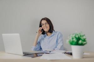 Beautiful female recruiter makes job offer to somene via cell phone, checks curriculum vitae on laptop computer, expalins detailes and pluses of work, surrounded with flower and personal diary photo