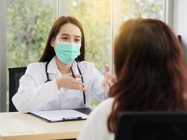 A female doctor or nurse with a surgical mask is talking or interview a middle-aged female patient, ideas for healthcare concepts. photo