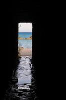 Afternoon view through an opening of an underpass of the rocks and beach around Petra tou Romiou, in Paphos, Cyprus. photo