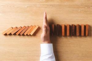 Risk management and business strategy concept, businessman hands stop the dominoes from falling continuously, preventing future risks from crisis. photo