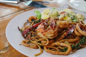 Asian woman eating spaghetti with spicy seafood sauce in a restaurant. The spicy seafood spaghetti was served in a plate and placed on the dining table as the woman ordered. photo