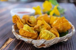 Crispy dumplings wrapped in chicken, vegetables and spices are served in a white plate placed on a wooden table inside the restaurant. Fried dumplings are popular for their delicious taste. photo