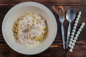 spaghetti carbonara, a delicious mix of ham, bacon and hot cheese, served in a white plate on a ready to eat wooden table. Delicious spaghetti with carbonara sauce mixed with ham, bacon and cheese. photo