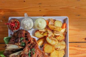 German pork knuckle is served with baked potatoes and sauce inside a white ceramic plate placed on the dining room table to make the pork knuckle ready for a dinner feast. photo