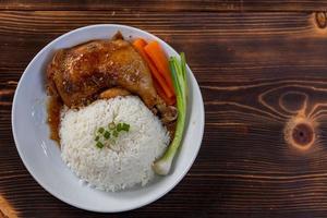 Roasted chicken thighs and drumsticks are served with jasmine rice and fresh vegetables in a white plate. Chicken thighs baked in sweet and delicious sauce are served with hot steamed rice on a plate. photo