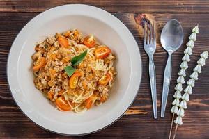 Spaghetti stir-fried with tomato sauce and minced chicken in hot Thai style. Tender and delicious served in a white plate placed on a wooden table, resulting in a delicious spaghetti from the sauce. photo