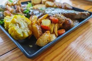 el bistec de ternera a la parrilla con salsa se sirve con una ensalada de frutas y verduras dentro de un plato de cerámica negra en la mesa del comedor para preparar el bistec para una cena festiva. foto