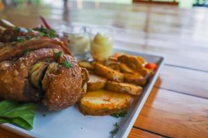 German pork knuckle is served with baked potatoes and sauce inside a white ceramic plate placed on the dining room table to make the pork knuckle ready for a dinner feast. photo