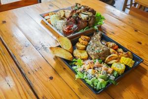 el bistec de ternera a la parrilla con salsa se sirve con una ensalada de frutas y verduras dentro de un plato de cerámica negra en la mesa del comedor para preparar el bistec para una cena festiva. foto