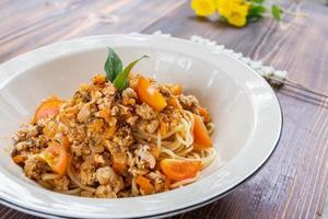 Spaghetti stir-fried with tomato sauce and minced chicken in hot Thai style. Tender and delicious served in a white plate placed on a wooden table, resulting in a delicious spaghetti from the sauce. photo