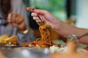 Asian woman eating spaghetti with spicy seafood sauce in a restaurant. The spicy seafood spaghetti was served in a plate and placed on the dining table as the woman ordered. photo