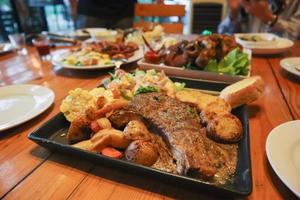 Grilled beef steak with gravy is served with a fruit and vegetable salad inside a black ceramic plate on the dining room table to prepare the steak for a festive dinner. photo