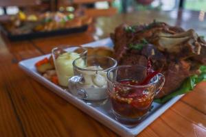 German pork knuckle is served with baked potatoes and sauce inside a white ceramic plate placed on the dining room table to make the pork knuckle ready for a dinner feast. photo