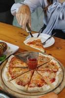 una joven está feliz de ver la comida en la mesa y elegir el menú de pizza para comer con buen gusto. los menús de pizza son perfectos para banquetes entre amigos y familiares ya que son cómodos para comer foto