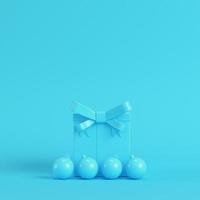 Gift box with ribbon bow and christmas ball on bright blue background in pastel colors photo