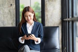 Asian businesswoman in formal suit in office happy and cheerful during using smartphone and working, copy space. photo