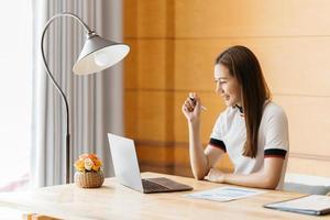 mujer joven sonriente usando laptop, sentada en el sofá en casa, hermosa chica comprando o chateando en línea en las redes sociales, divirtiéndose, viendo películas, freelancer trabajando en un proyecto de computadora foto