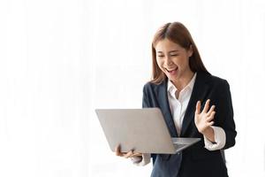 Portrait of an excited young asian business woman holding laptop computer and celebrating success isolated over white background, copy space. photo