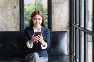 Asian businesswoman in formal suit in office happy and cheerful during using smartphone and working, copy space. photo