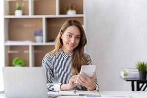 Portrait of asian business woman paying bills online with laptop in office. Beautiful girl with computer and chequebook, happy paying bills. Startup business financial calculate account concept photo