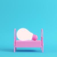 Pink single bed with glowing light bulb on bright blue background in pastel colors photo