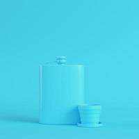 Hip flask with cup on bright blue background in pastel colors. Minimalism concept photo