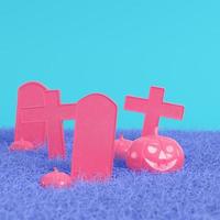 Pink halloween pumpkins with crosses and gravestones on bright blue background in pastel colors. Minimalism concept photo