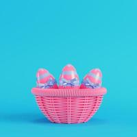 Pink easter eggs with bow in a wicker basket on bright blue background in pastel colors photo