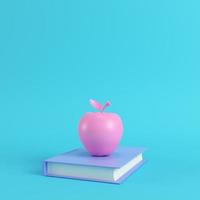 Pink apple on a book on bright blue background in pastel colors photo