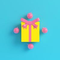 Yellow gift box with ribbon bow and christmas ball on bright blue background in pastel colors