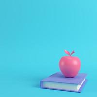 Pink apple on a book on bright blue background in pastel colors photo