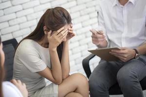 Frustrated young business woman and unhappy holding head in hands at psychotherapy session , psychiatrist making notes diary at working  office photo