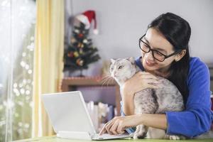 Happy young asian woman online using laptop while connection on video call , Beautiful woman speaking looking at camera talking with her friend video call and cute cat resting at home photo