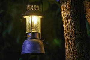 lámpara de aceite antigua colgada de un árbol en el bosque en la atmósfera de campamento de la noche. imagen del concepto de viaje al aire libre. enfoque suave.