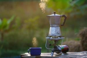 cafetera moka antigua en la estufa de gas para acampar cuando sale el sol por la mañana. enfoque suave. foto