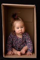 Happy little girl sitting in a cardboard box and having fun photo