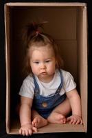 Happy little girl sitting in a cardboard box and having fun photo