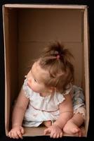 Happy little girl sitting in a cardboard box and having fun photo