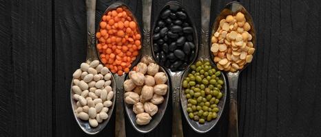 Variety of legumes in old silver spoons on a black wooden background. photo