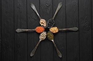 Variety of legumes in old silver spoons on a black wooden background. photo