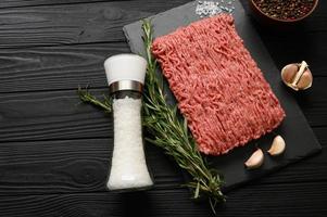 Fresh raw meat or ground chicken meat on a wooden cutting board with thyme, spices and garlic. Rustic wooden background. Top view. Copy space. photo