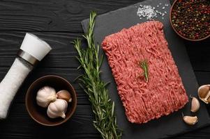 Fresh raw meat or ground chicken meat on a wooden cutting board with thyme, spices and garlic. Rustic wooden background. Top view. Copy space. photo