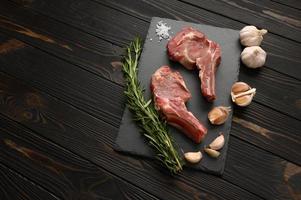 Raw cowboy steak and spices on a black wooden background. photo