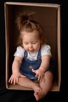 Happy little girl sitting in a cardboard box and having fun photo