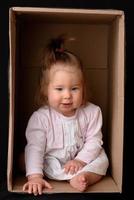 Happy little girl sitting in a cardboard box and having fun photo