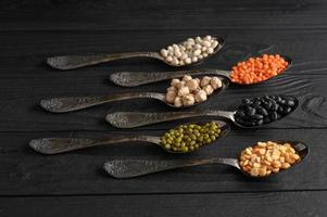 Variety of legumes in old silver spoons on a black wooden background. photo