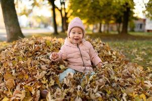 una niña juega en un montón de follaje otoñal. foto